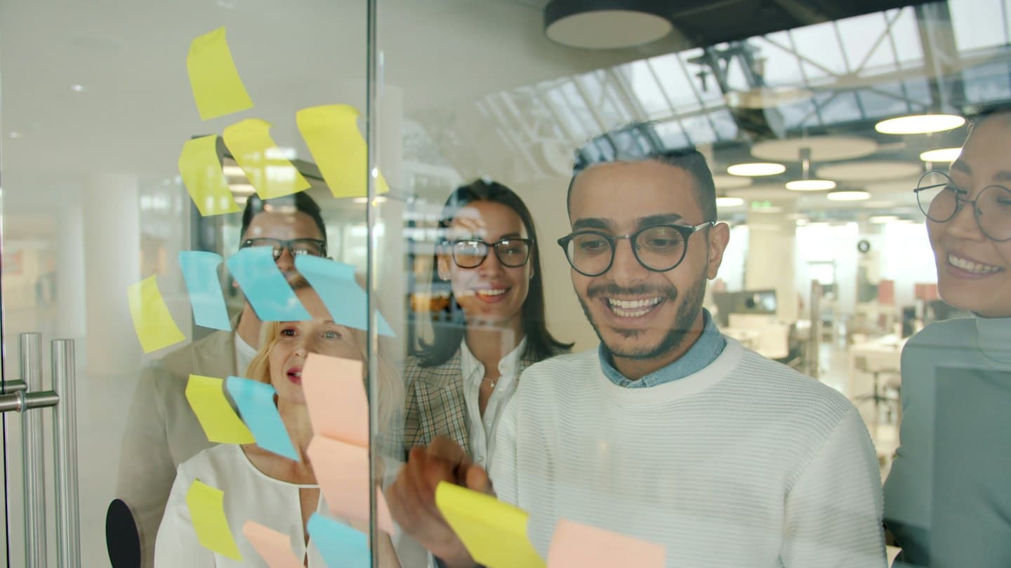 Business people brainstorm ideas on a glass board with sticky notes.
